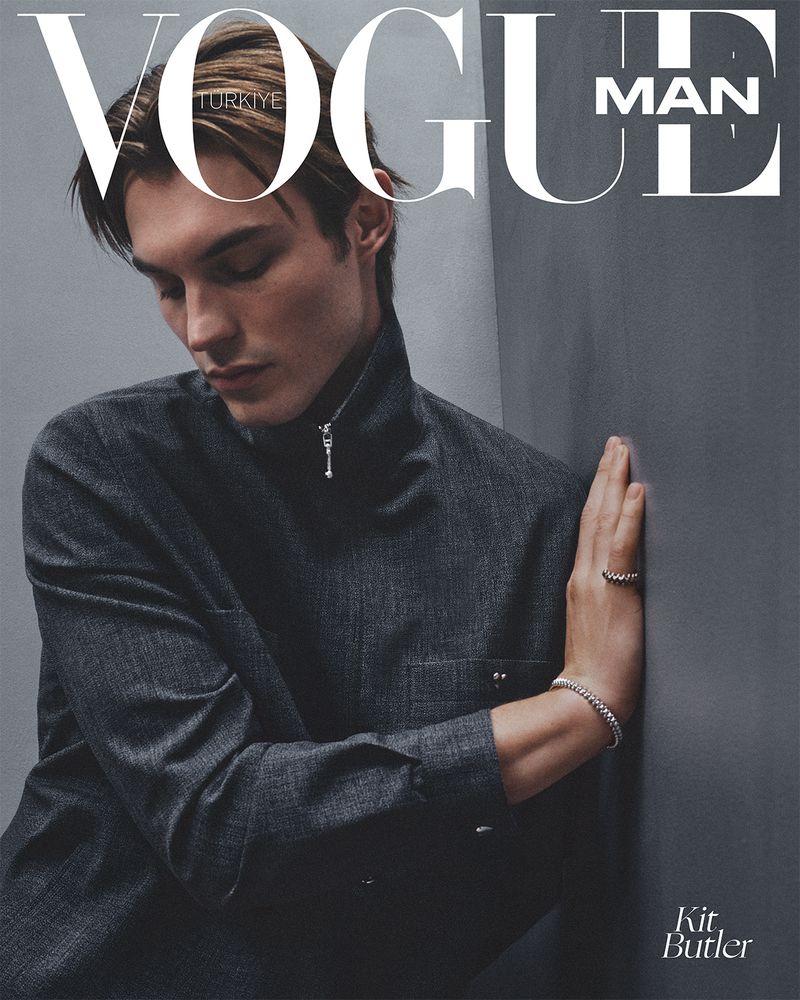 Vogue Man magazine cover featuring a young adult male model wearing a dark gray collared shirt, silver bracelets and a ring indoors.