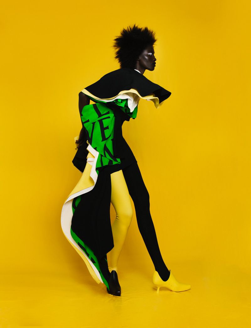 Model Sokhna Cisse wearing structured black, green, and yellow apparel against a solid yellow background for Citizen K International.