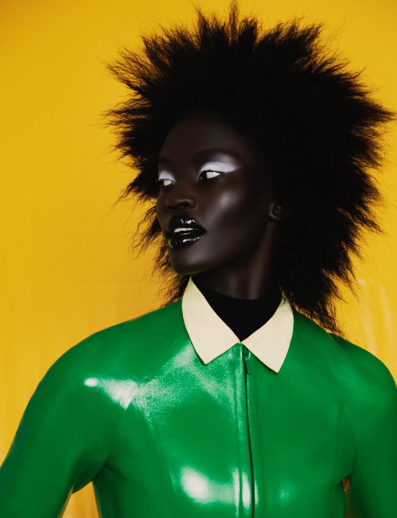 Model with spiky black hair wearing a green top with white collar against a yellow background for Citizen K International.