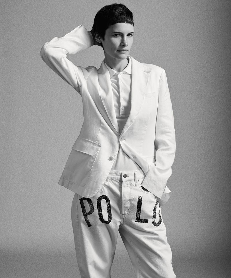 Model Camille Desjardins posing in a white tailored blazer, white polo shirt, and white trousers with stenciled lettering.