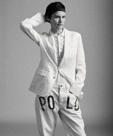 Model Camille Desjardins posing in a white tailored blazer, white polo shirt, and white trousers with stenciled lettering.