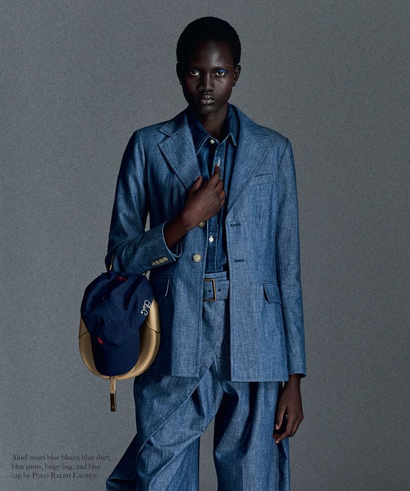 Model wearing a blue denim suit holding a blue cap against a neutral grey background