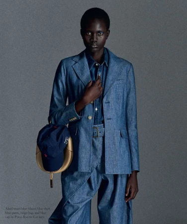 Model wearing a blue denim suit holding a blue cap against a neutral grey background