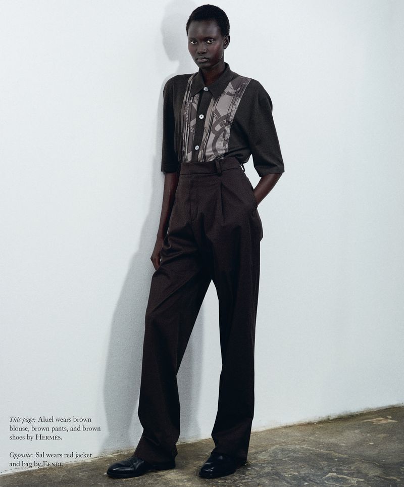 Model Aluel Keror standing against a plain white wall wearing a dark brown blouse and high-waisted trousers for Mission Magazine.