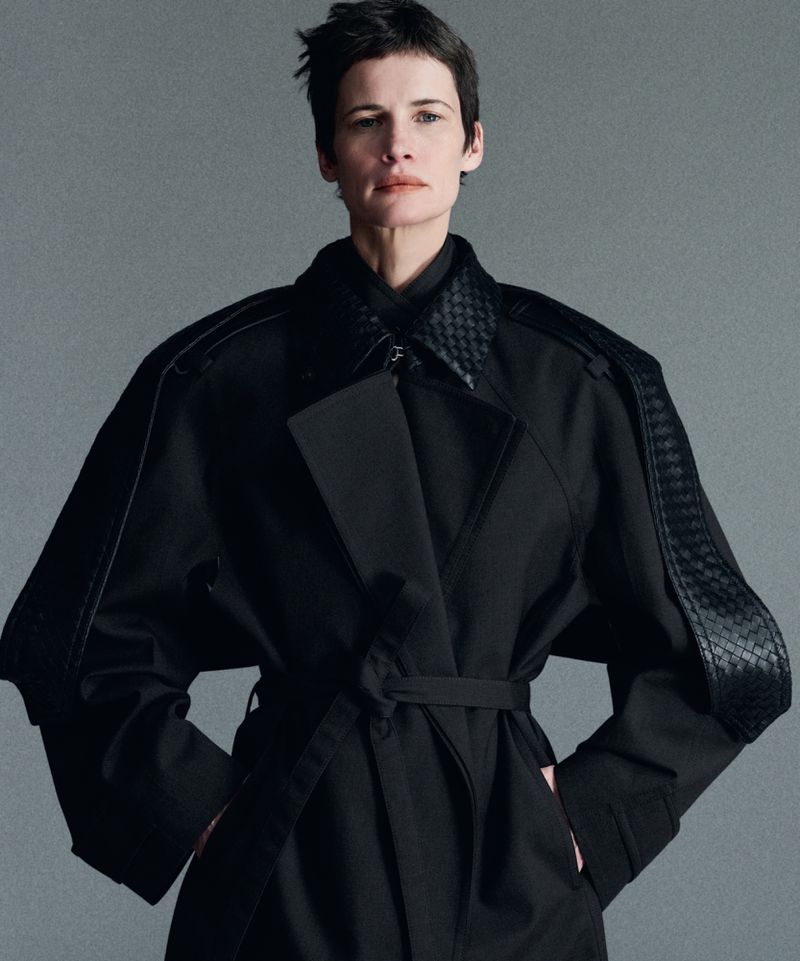 Model with short dark hair wearing a black trench coat against a grey studio backdrop for Mission Magazine.