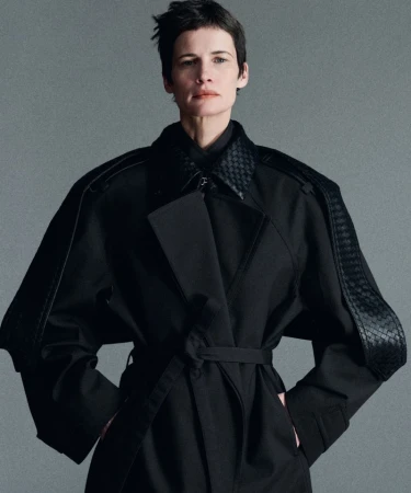 Model with short dark hair wearing a black trench coat against a grey studio backdrop for Mission Magazine.