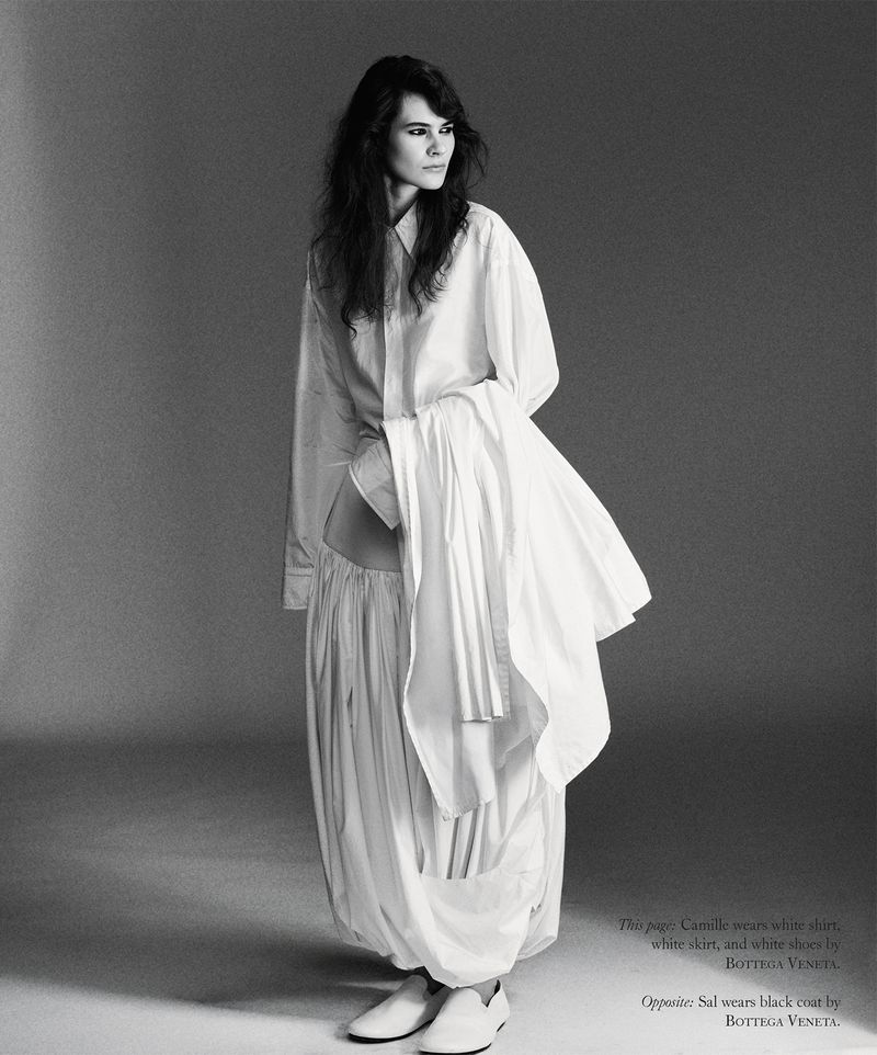 Model in loose white shirt and matching voluminous pleated skirt standing against a grey studio backdrop