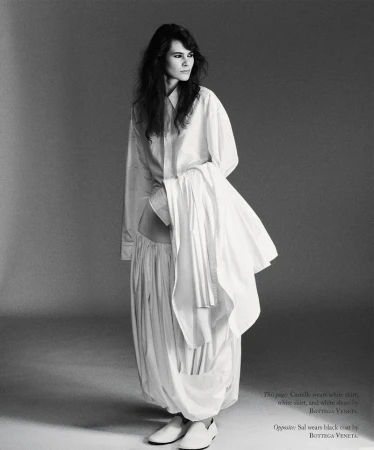 Model in loose white shirt and matching voluminous pleated skirt standing against a grey studio backdrop