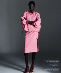 Model Aluel Keror wearing a pink zip jacket and pink skirt with arms crossed against a grey studio backdrop