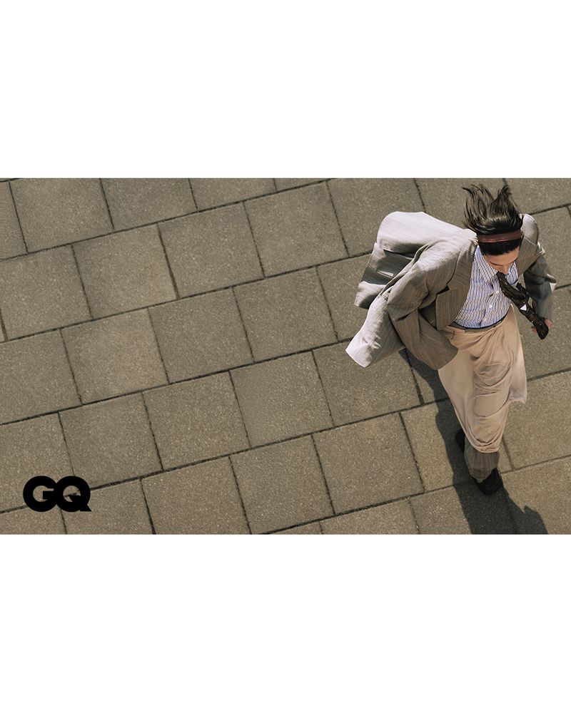 High-angle shot of a person in a suit and tie with a blindfold, running on a tiled surface, wearing a light-colored suit, tie and dress shoes.