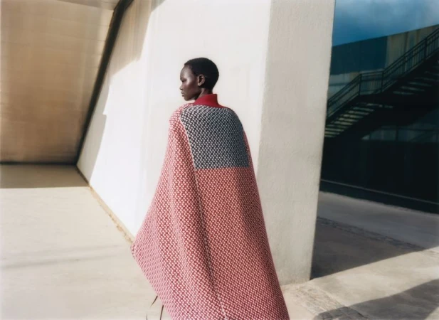 Model wearing patterned red cape standing outdoors near concrete architecture in Vogue Polska editorial