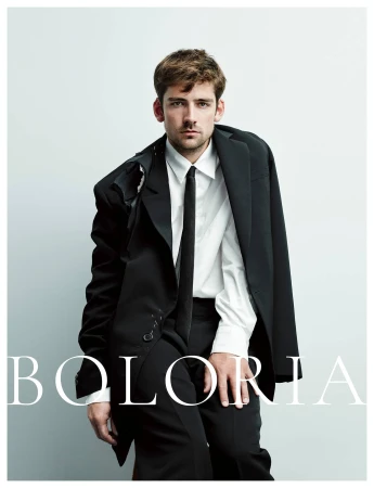 Man wearing a black suit jacket, white button-down shirt, and black tie against a seamless white background with Boloria text