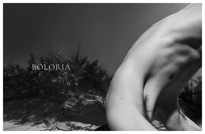 Black and white photograph of an arched torso close-up against sand dunes and coastal vegetation with Boloria branding.