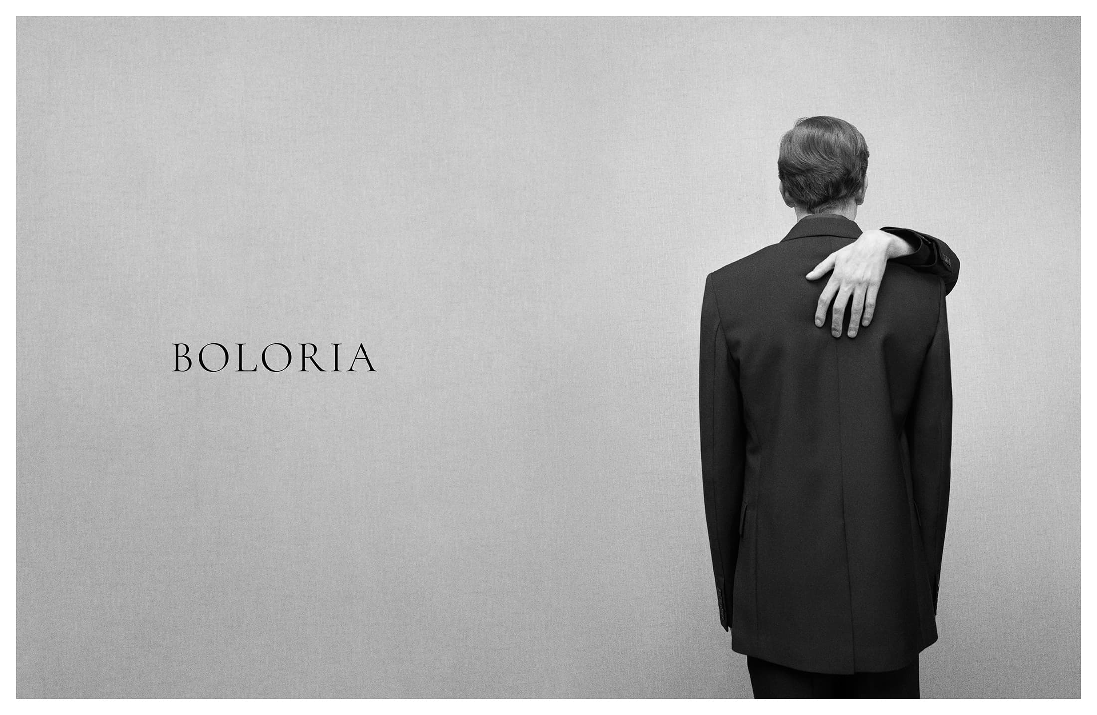Monochrome ad campaign image featuring a person in a dark suit with an unfamiliar hand resting on their back
