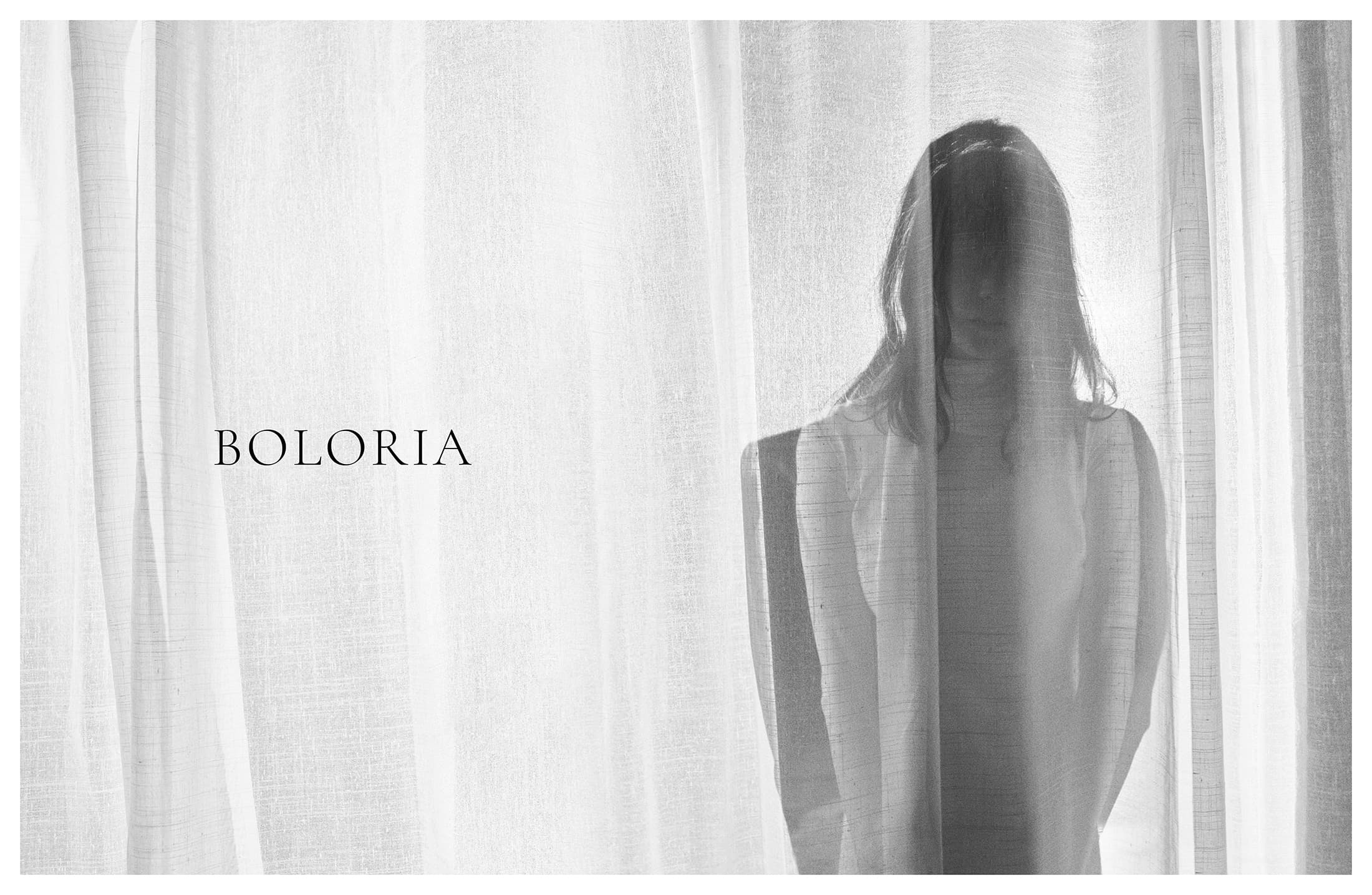 Monochrome image of a woman standing behind translucent white sheer curtains with the Boloria brand logo on the left