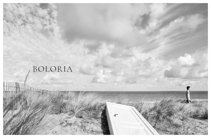 Monochrome landscape with sand dunes, an ocean horizon, a resting door, and a distant figure standing near the beach.