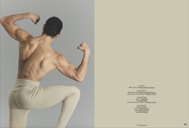 Back view of a shirtless muscular man posing in cream ribbed tights against a grey background on a magazine spread.