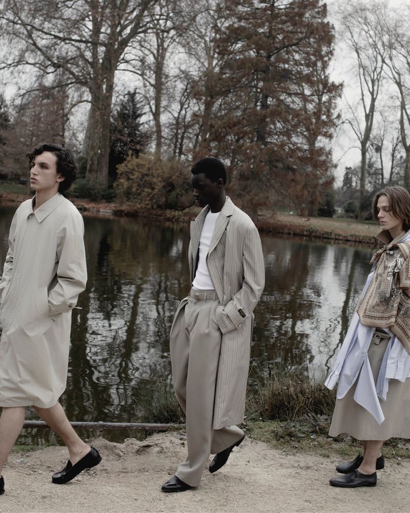 Three models walking along a park path beside a reflective pond under overcast skies for The Greatest Magazine.