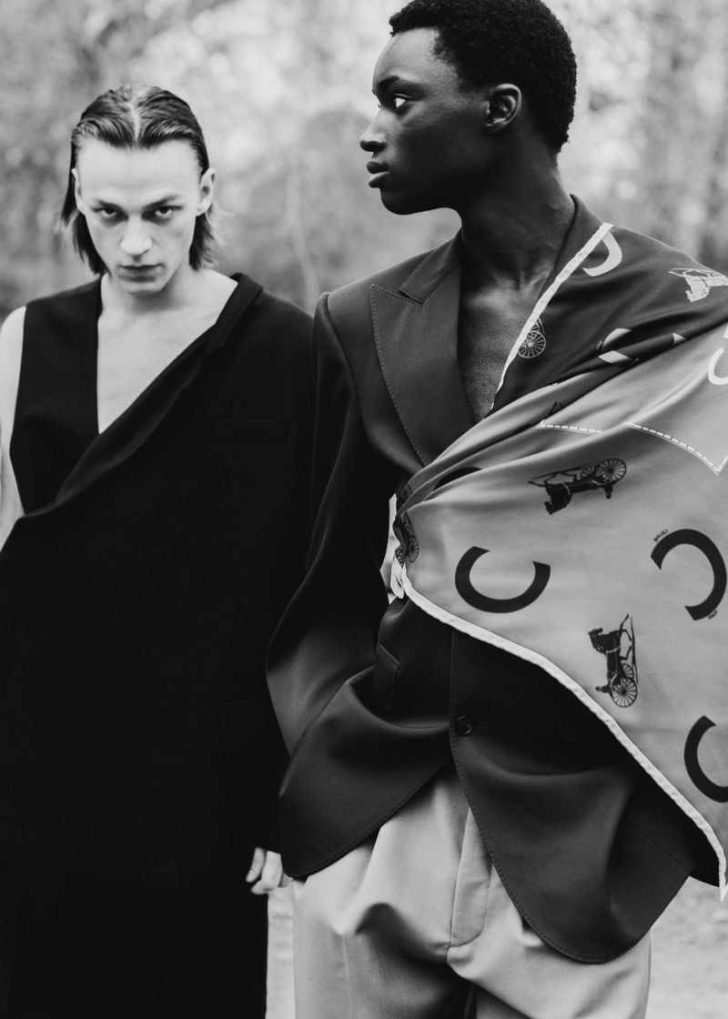 Black and white editorial portrait of two male models outdoors wearing tailored menswear and a printed silk scarf.