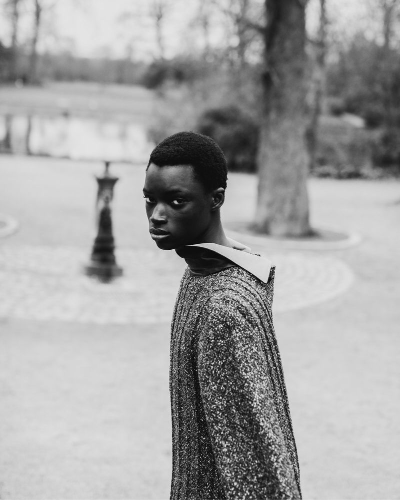 Black male model looking over his shoulder wearing a patterned textured sweater outdoors in a park
