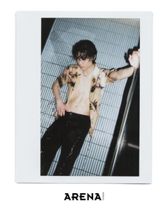 Polaroid photograph of a wet male model wearing an unbuttoned patterned short-sleeve shirt and dark trousers against a tiled wall