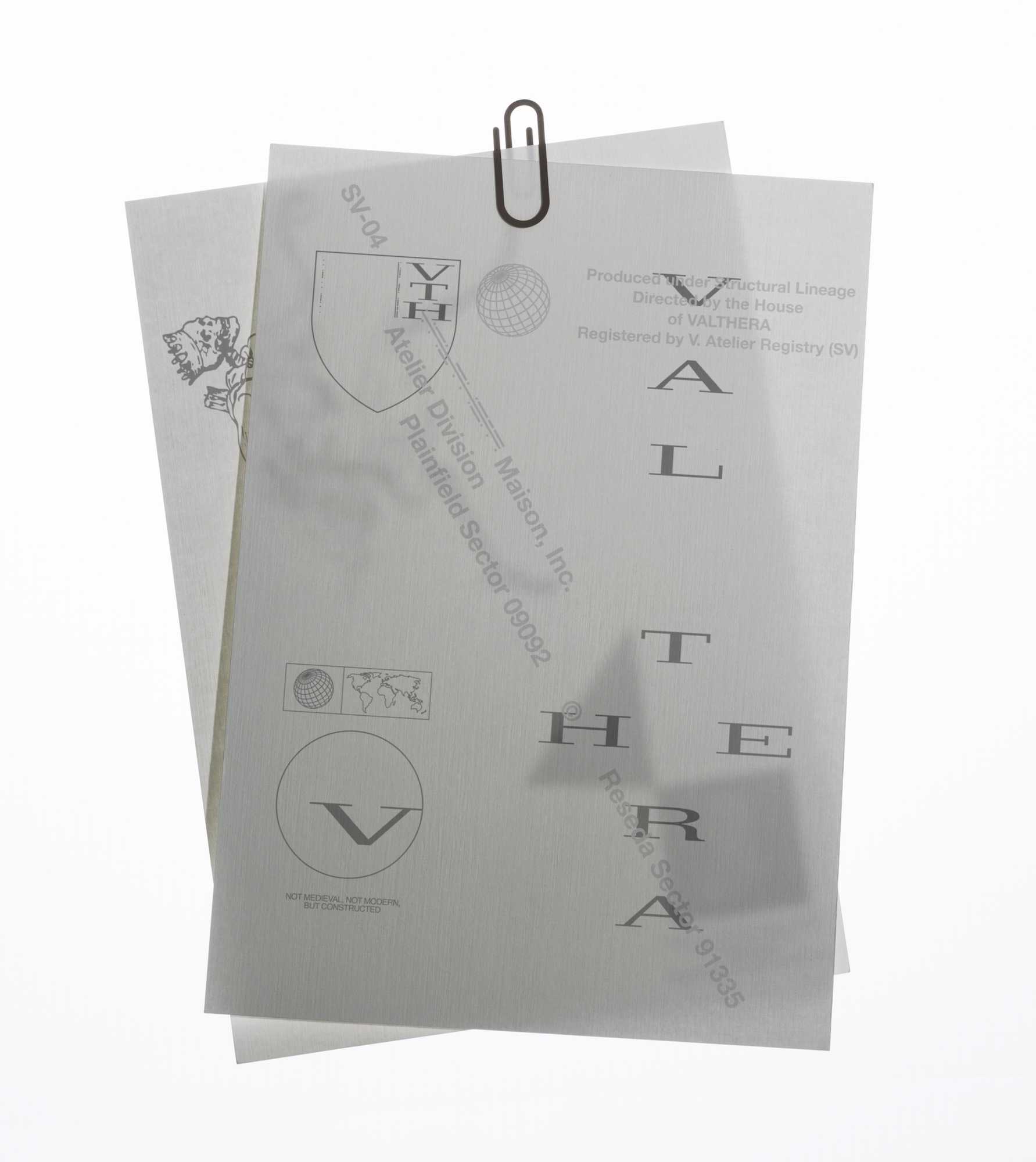 Close-up studio shot of two sheets of white paper clipped together with a metal paperclip, featuring architectural designs and logos.
