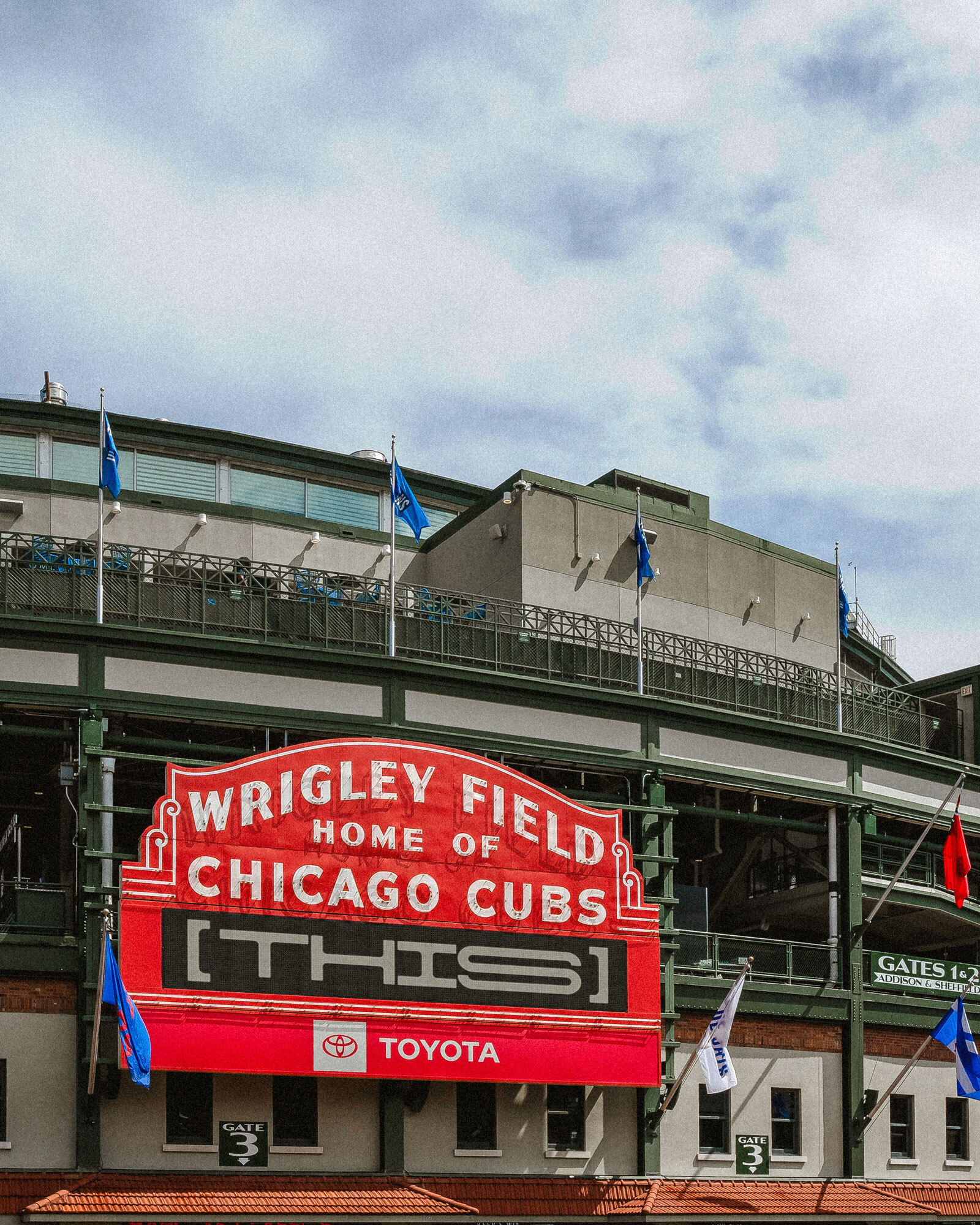 The iconic red Wrigley Field marquee sign outside the Chicago Cubs stadium under a partly cloudy sky.