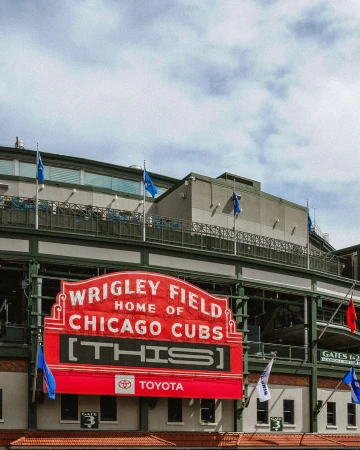 The iconic red Wrigley Field marquee sign outside the Chicago Cubs stadium under a partly cloudy sky.