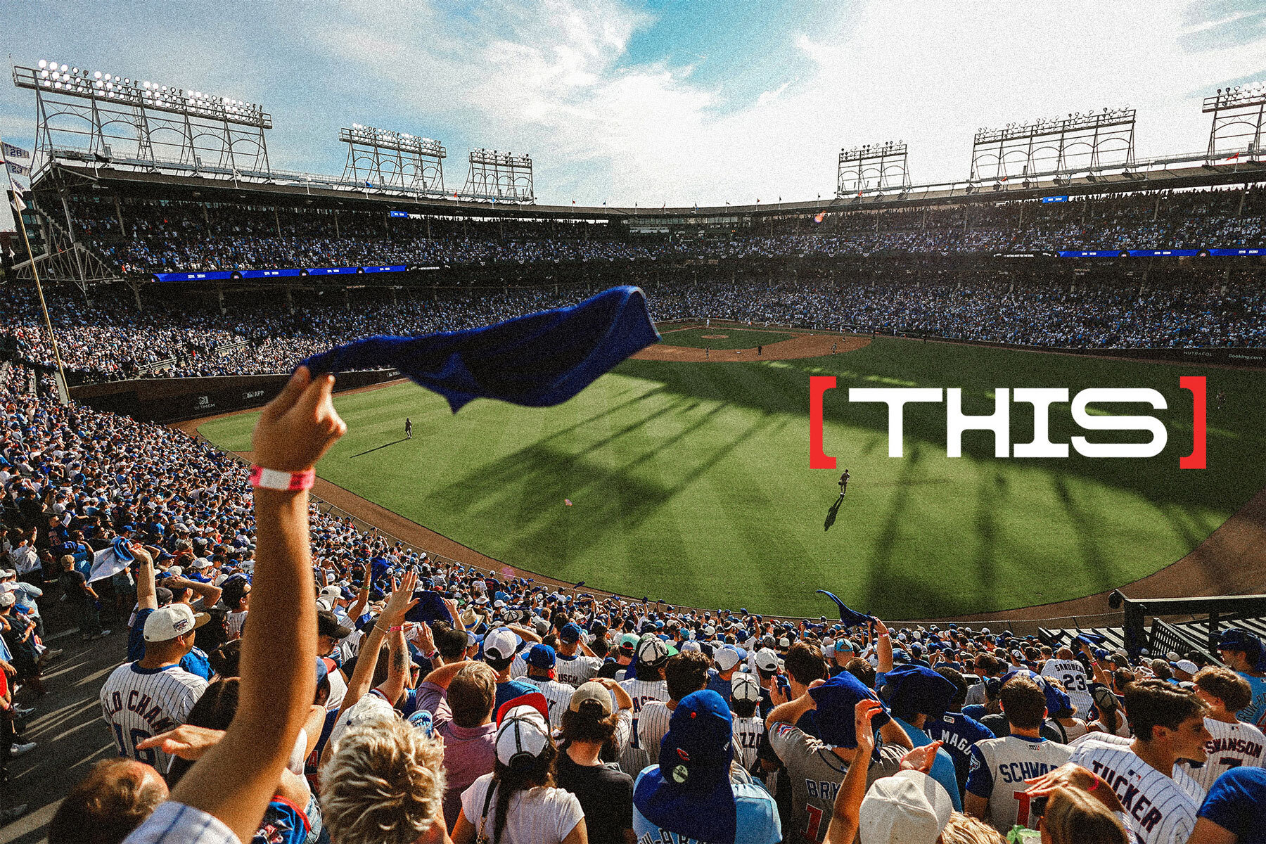 Wide view of a packed baseball stadium crowd cheering and waving blue rally towels during a Chicago Cubs game.