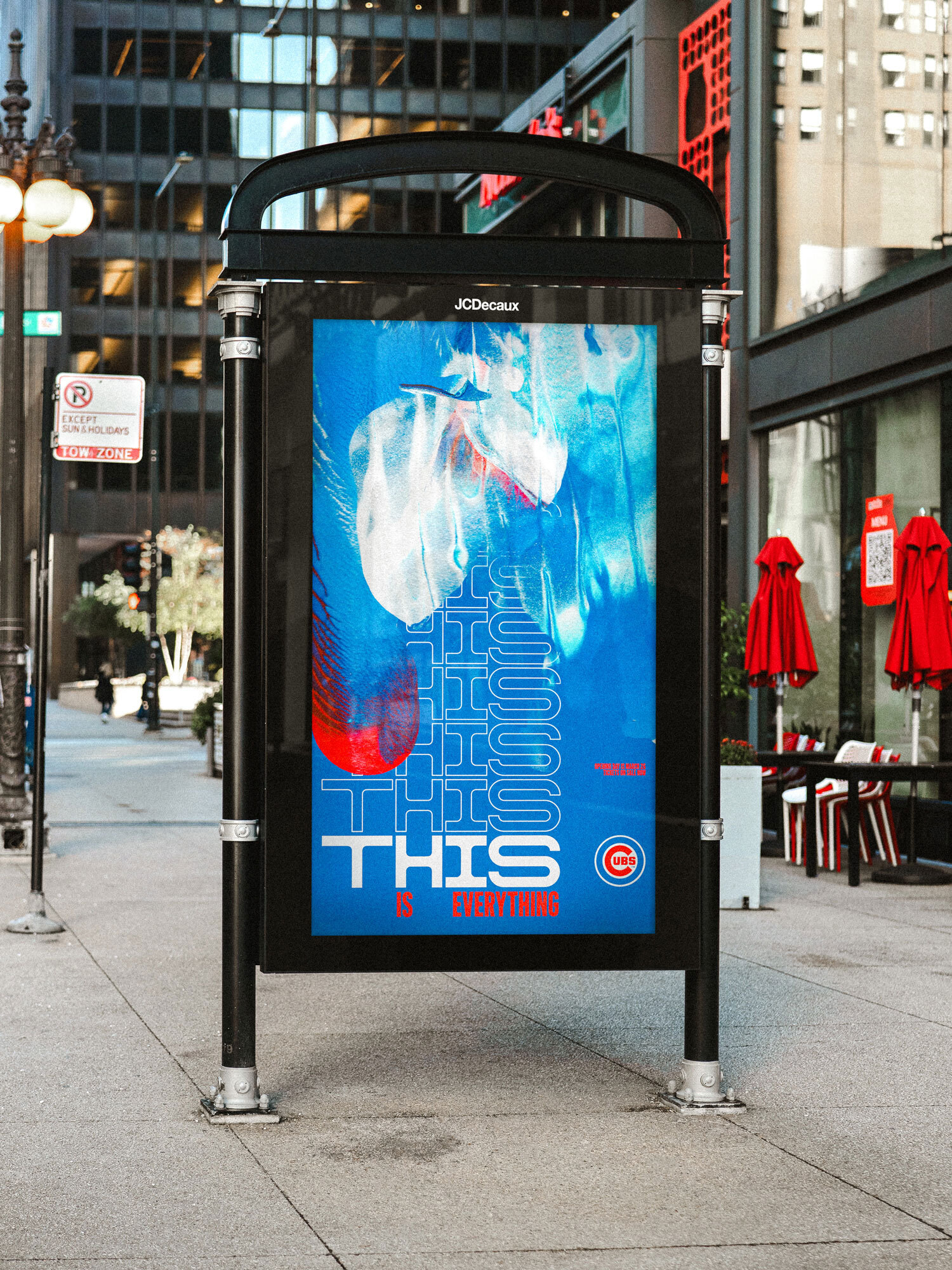 A black outdoor advertising kiosk displays a blue and red Chicago Cubs graphic poster on an urban sidewalk.