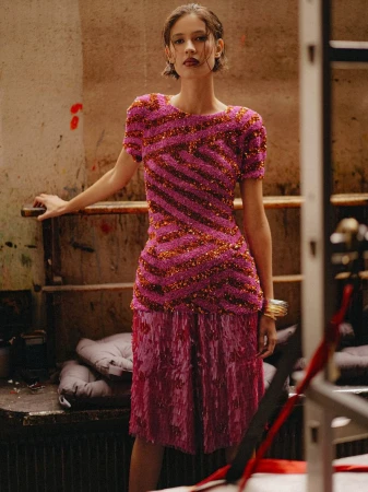 Model posing in a short-sleeve striped sequin top and magenta fringe skirt against a rustic studio backdrop.