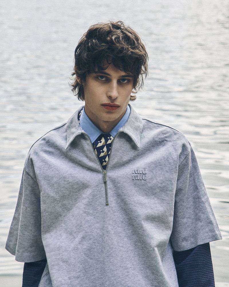 Model Federico Battisti in a grey zip polo shirt over a light blue collared shirt and tie against a water backdrop.