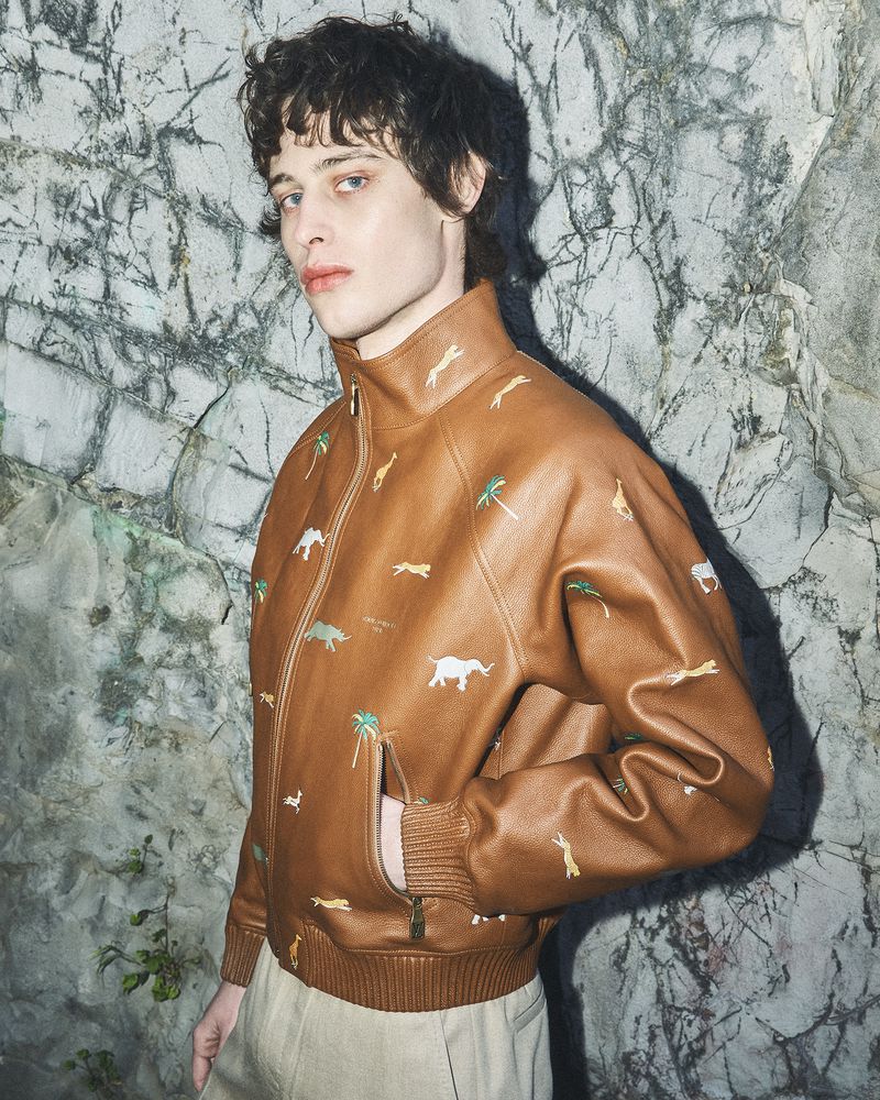 Model Federico Battisti wearing an embroidered brown leather jacket against a rocky cliff wall for Grey Magazine.