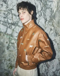 Model Federico Battisti wearing an embroidered brown leather jacket against a rocky cliff wall for Grey Magazine.
