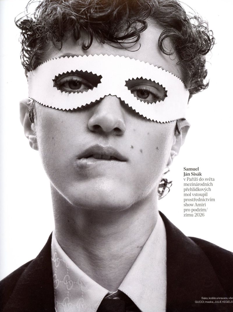 Close-up portrait of a young male model wearing a white paper mask over his eyes and a tailored suit jacket, for Vogue Czechoslovakia.
