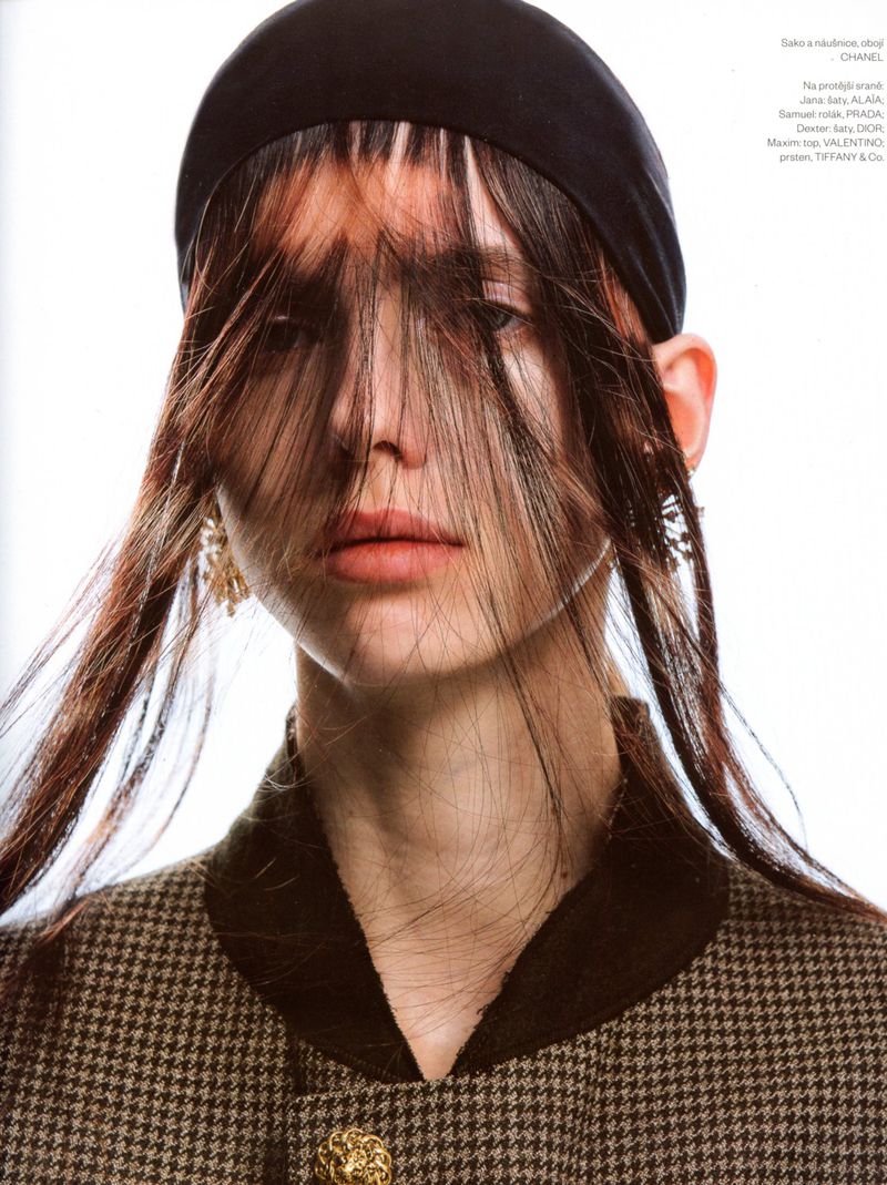 Close-up portrait of a model wearing a black headband and a patterned houndstooth jacket with hair covering eyes against a white background.