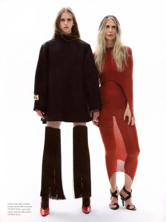 Two models posing against a white seamless backdrop, one in an oversized black coat with fringe legwear and one in a fitted rust knit dress.