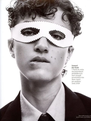 Close-up portrait of a young male model wearing a white paper mask over his eyes and a tailored suit jacket, for Vogue Czechoslovakia.