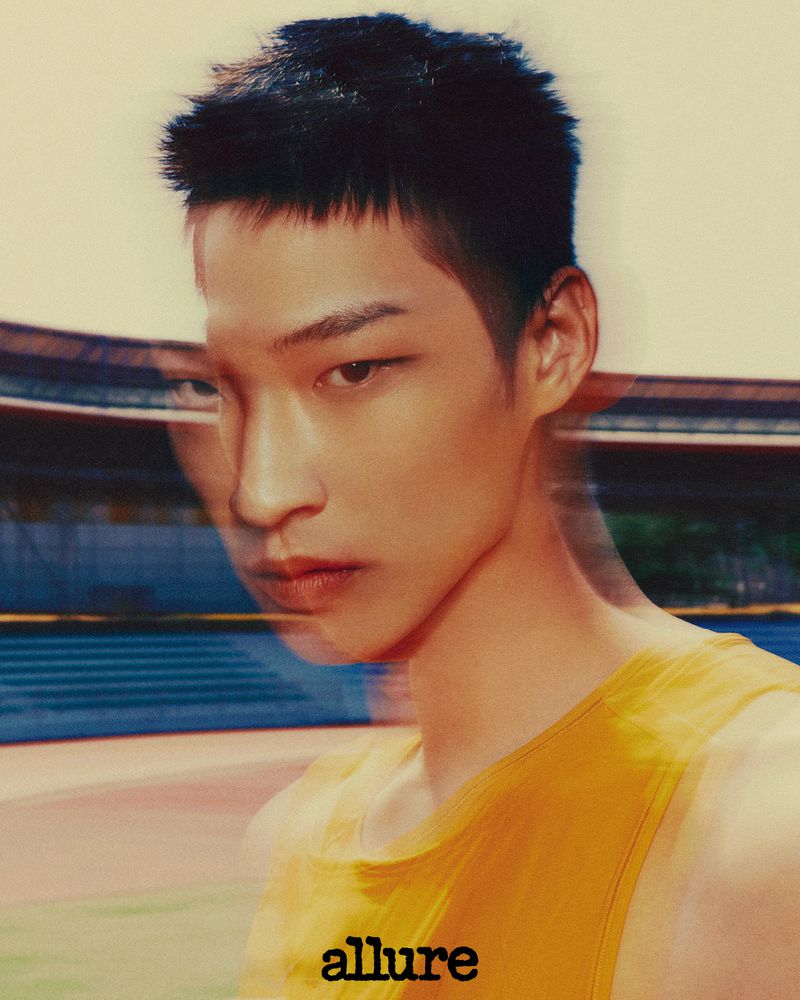 Portrait of an Asian male model with a blurry double exposure effect, wearing a yellow tank top, posing in an outdoor stadium.