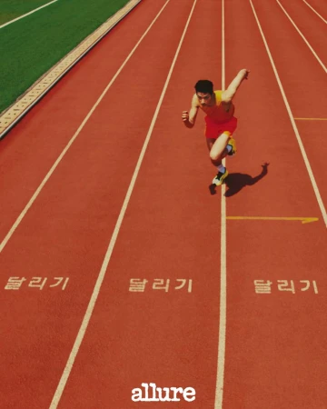 Man sprinting on a red running track outdoors, captured from a high angle with green field visible in the background, athletic shoes.