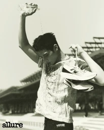 Monochrome fashion editorial image of a male model pouring water over his head while holding running shoes