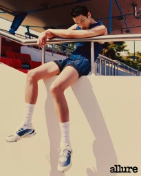 Model wearing blue denim apparel and white sneakers leaning on a stadium railing for Allure Korea editorial