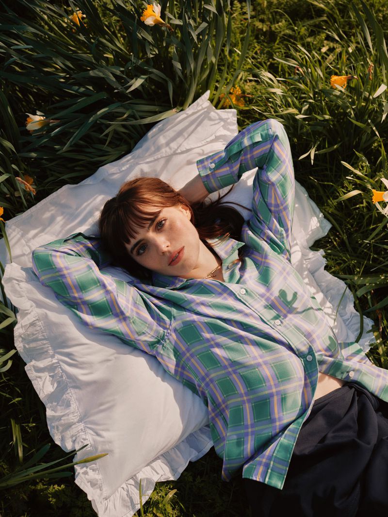 Bella Maclean lying on a white pillow in a grassy field wearing a green plaid shirt for Telegraph Luxury