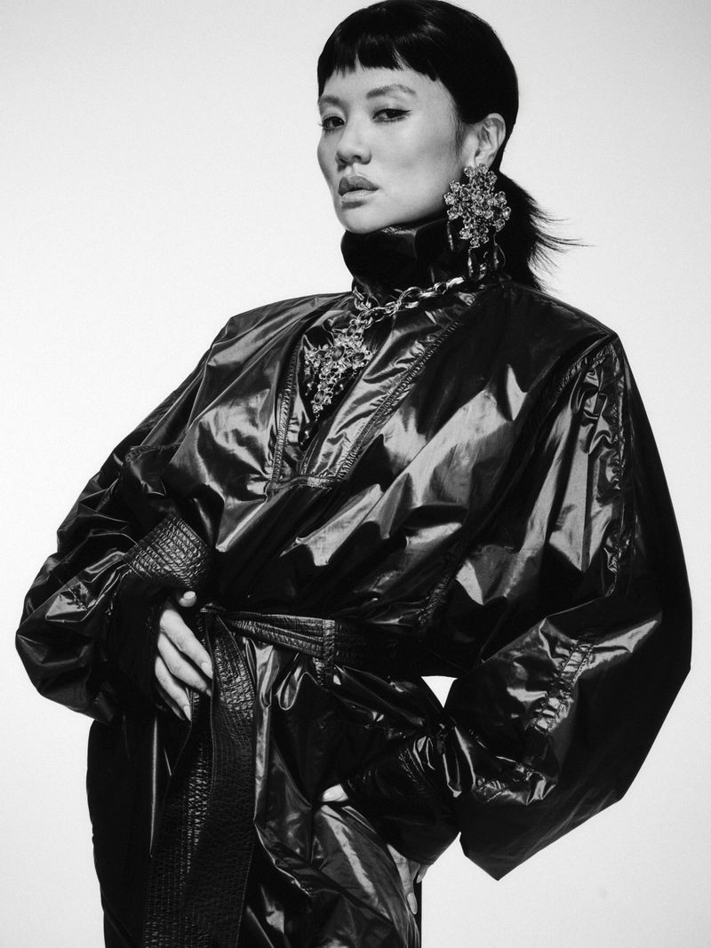 Portrait of Rei Ami in a glossy black jacket and statement earrings against a plain light background for Numero Netherlands.