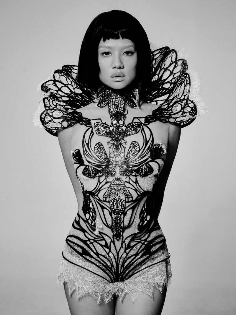Portrait of a woman wearing an intricate black structural lace bodysuit against a grey background