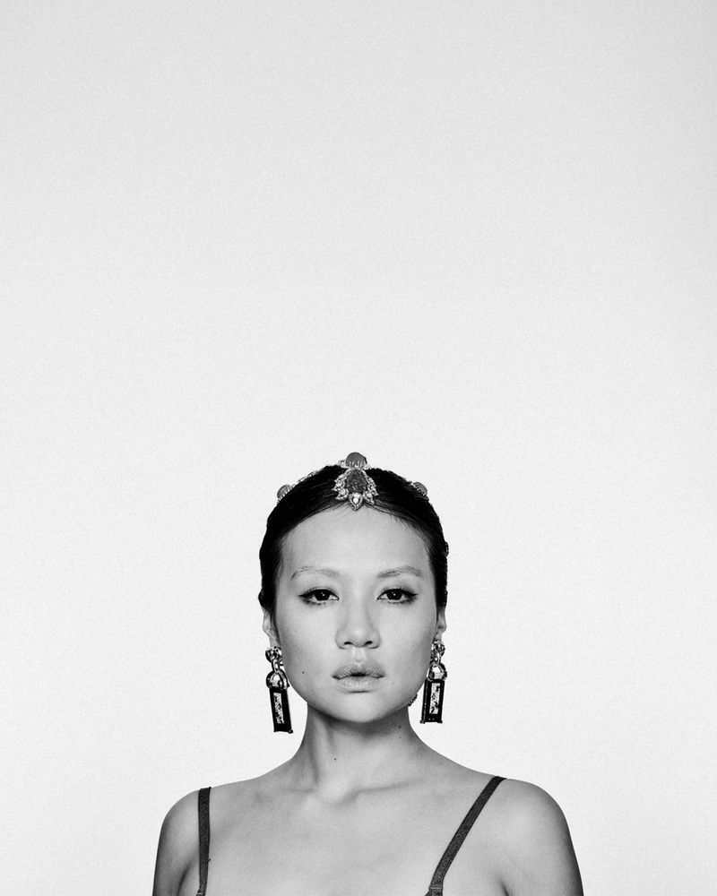 Portrait of a woman wearing statement earrings and a jewelled headpiece against a plain white background