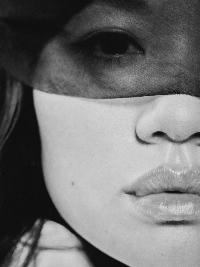 Black and white close-up portrait of a woman with a dark sheer band covering her eyes.