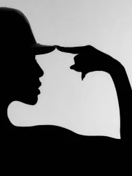 Black silhouette profile of a woman wearing a cap and touching the brim with a pointed finger against a bright seamless background.