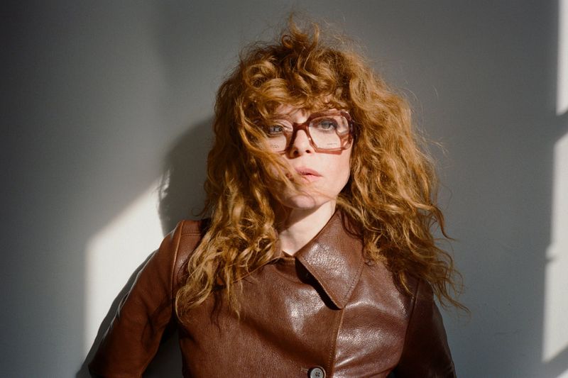 Natasha Lyonne in a brown leather jacket and glasses against a light wall, photographed by Matt Jones for M Revista de Milenio.
