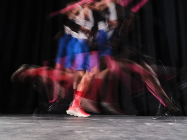Long exposure shot of an athlete running in vibrant sportswear and pink shoes against a dark background.